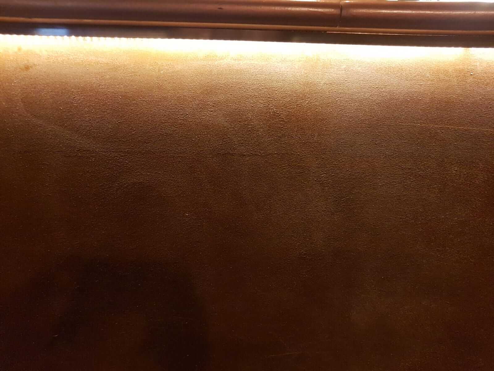 Dettaglio ravvicinato di una finitura decorativa spatolata nei toni del bronzo, illuminata da una luce radente