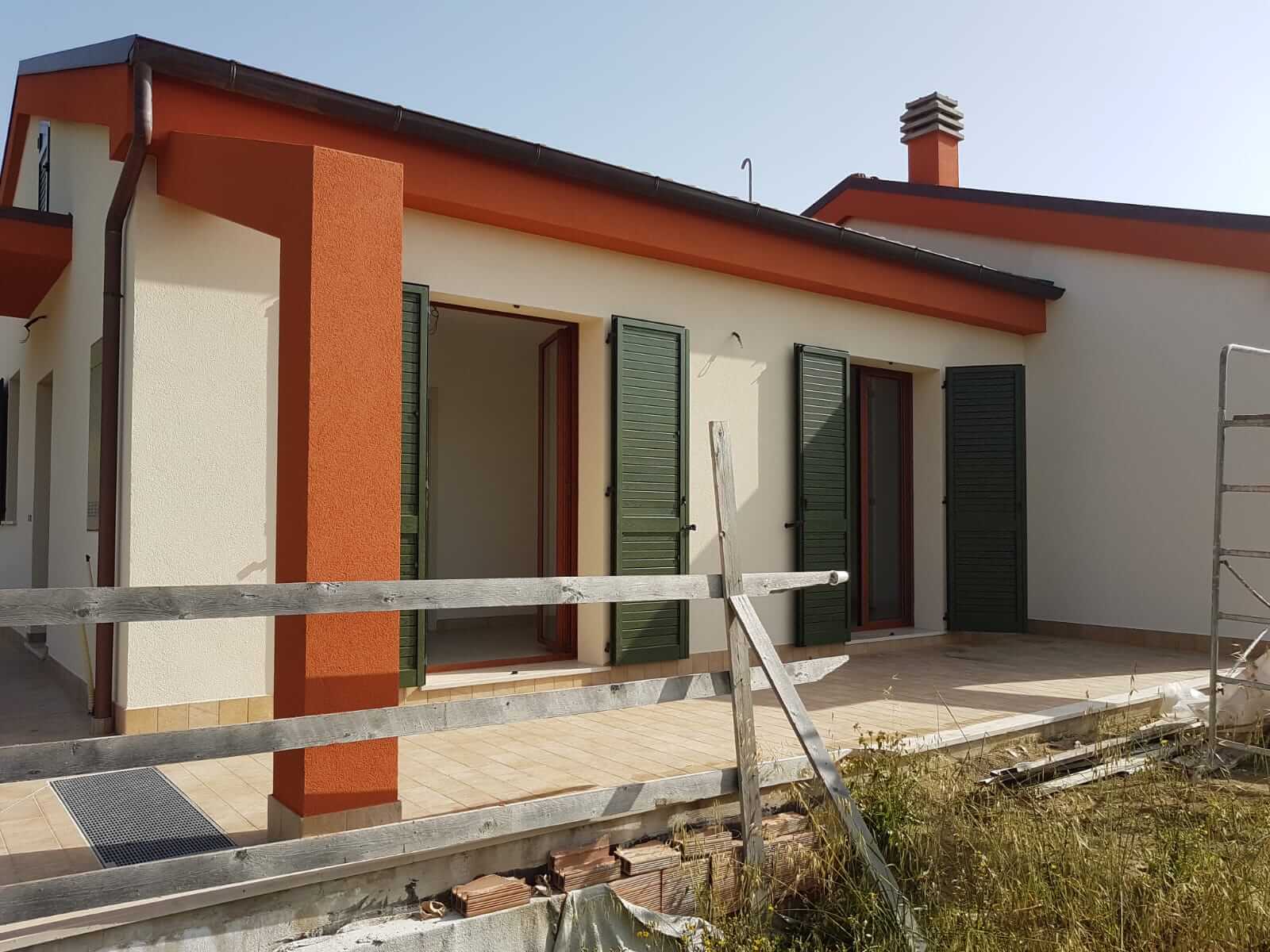 Dettaglio di un pilastro arancione a intonachino e del sottotetto di una villa, con persiane verdi aperte
