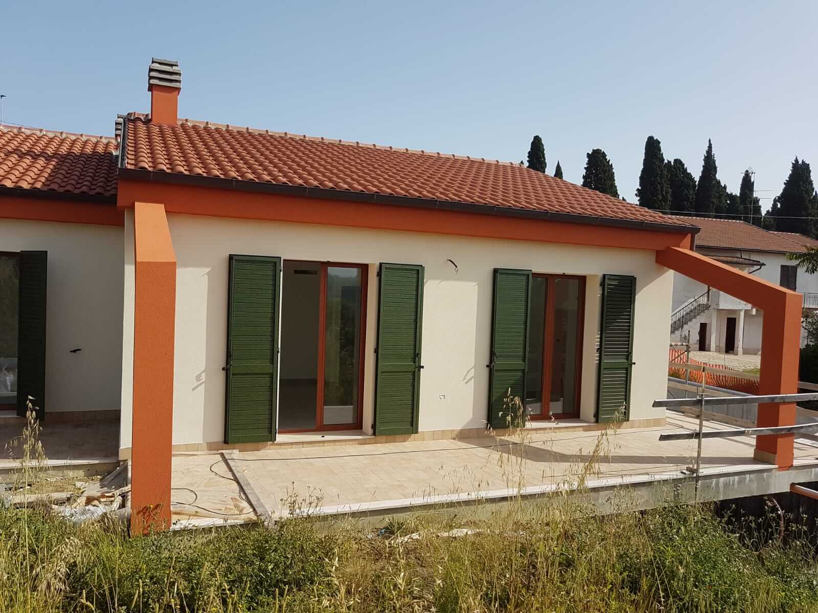 Portico di una villa con pilastri arancioni, pareti crema e persiane verdi, tetto in tegole