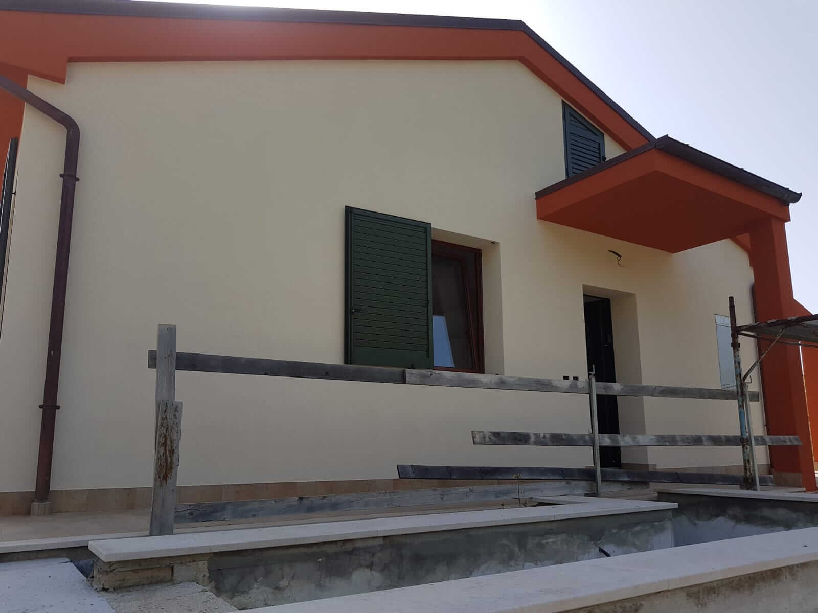 Prospetto laterale di una villa con parete crema uniforme e cornici arancioni lungo la linea del tetto