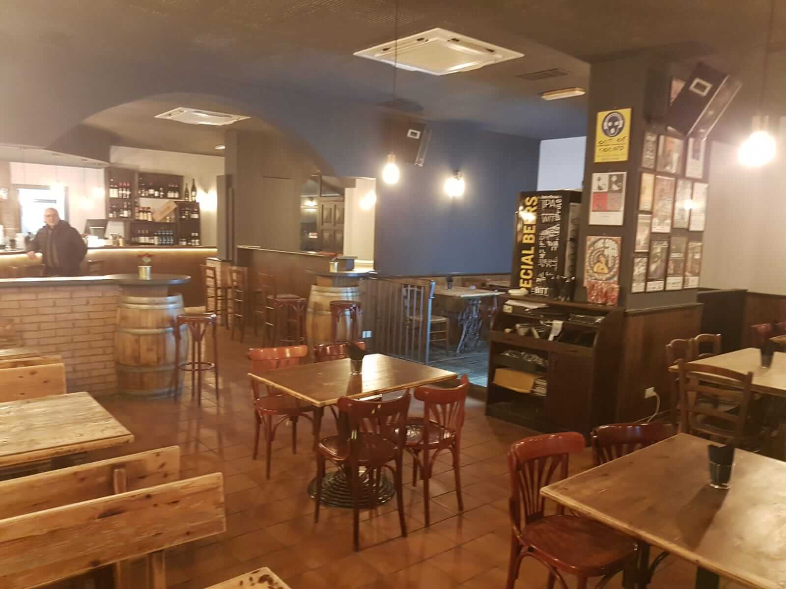 Sala di un locale con pareti tinteggiate in blu e grigio, soffitto a volta, mattoni a vista e tavoli in legno