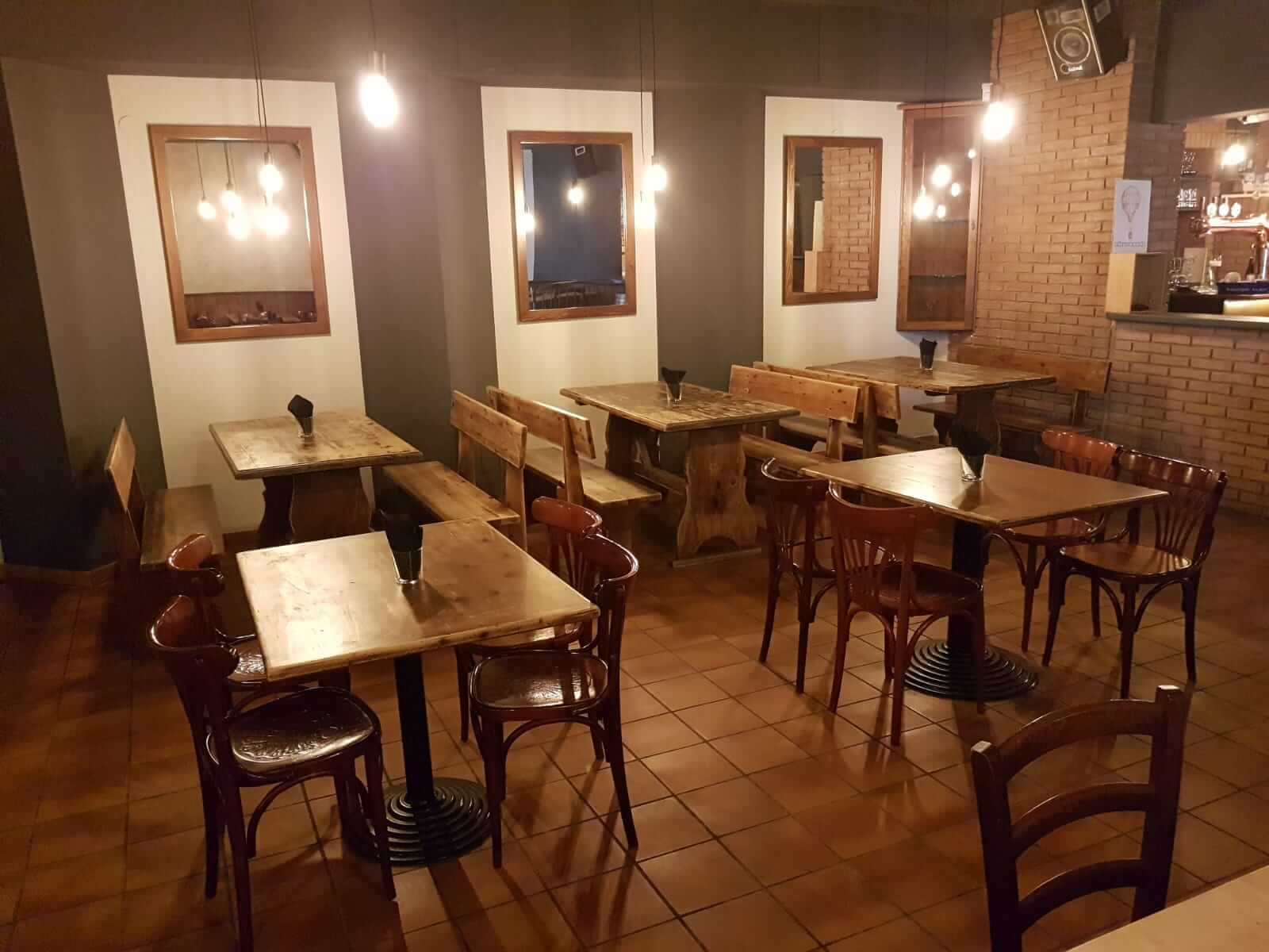 Sala di una birreria con pareti tinteggiate in grigio e bianco, cornici a specchio e tavoli in legno